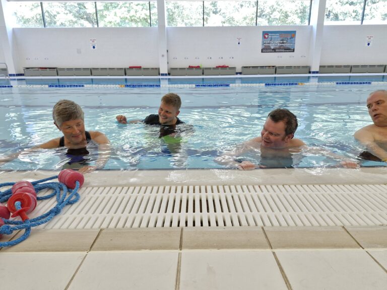 Three people in a swimming pool supported by a physiotherapist. The physiotherapist is supporting a woman while the others exercise next to her