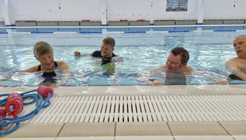 Three people in a swimming pool supported by a physiotherapist. The physiotherapist is supporting a woman while the others exercise next to her