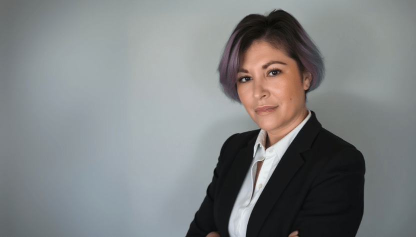 CEO Zoe Richardson in front of a soft grey background. Zoe is looking directly at the camera. She is wearing a white shirt with black blazer.