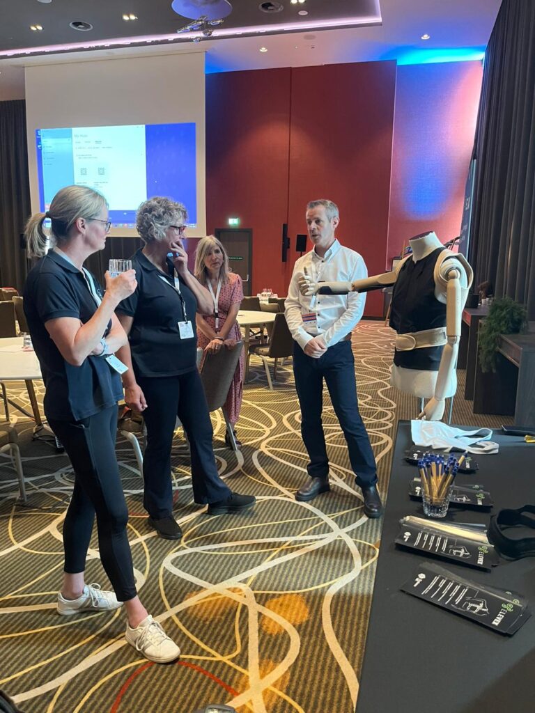 Lynn and Ulrike meeting with other FSHD Connect delegates. They are speaking with two people who have a stand with some equipment demos.