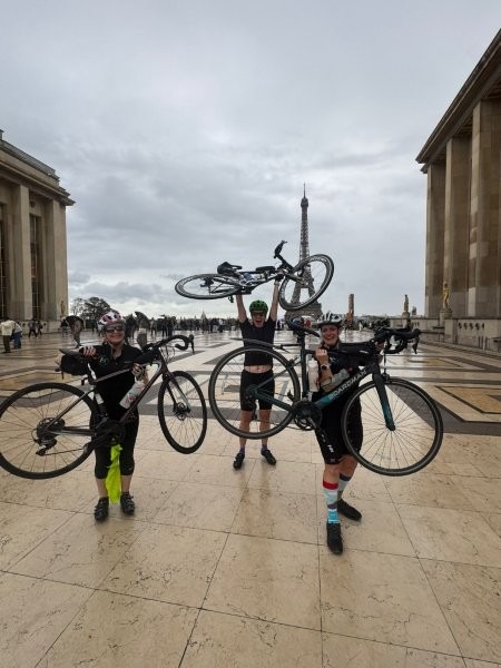 Three people in front of the Eiffel Tower lifting their bikes above their heads