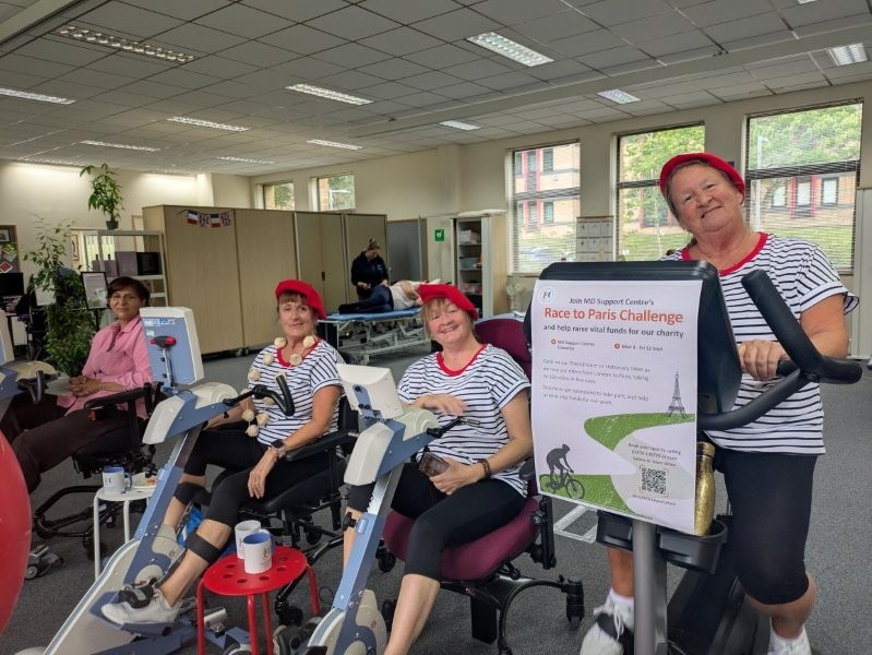 Four people using exercise bikes. Three are dressed in matching stripey outfits and berets.