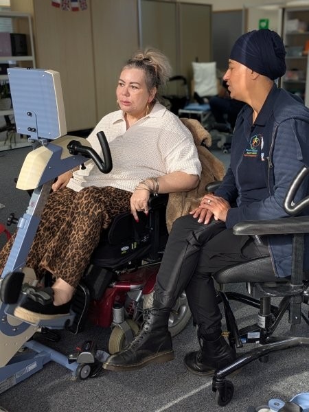 A woman using an accessible exercise bike supported by our therapy assistant