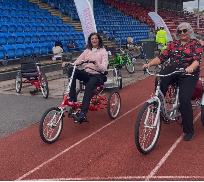 Two women using accessible three wheel bikes on a track
