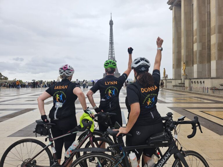 Sarah, Lynn, and Donna with their bikes in front of the Eiffel Tower. They have their back to the camera and are facing the tower with their hands raised in celebration,