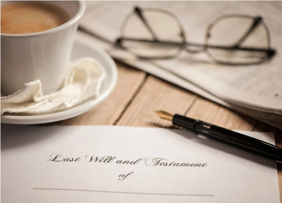 A close up of a table on which is a cup of tea, a pair of glasses, a fountain pen and a document entitled 'last will and testament of'