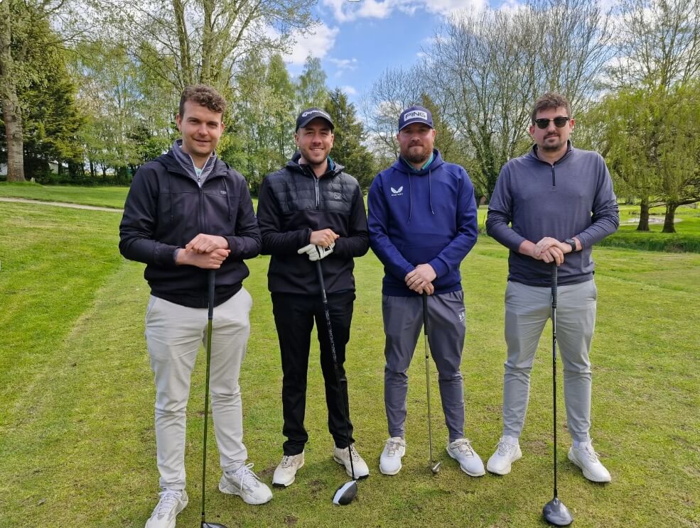 Four men standing on a golf course holding golf clubs