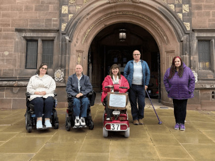 A group of people some in wheelchairs, others using scooters, and some standing, in front of a building in London