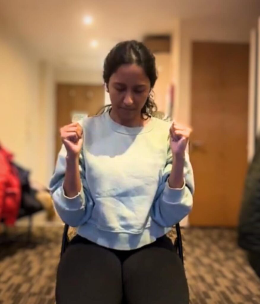 Rewati is seated in her living room with her eyes closed. Her hands are partially raised as if part way through a breathing stretch