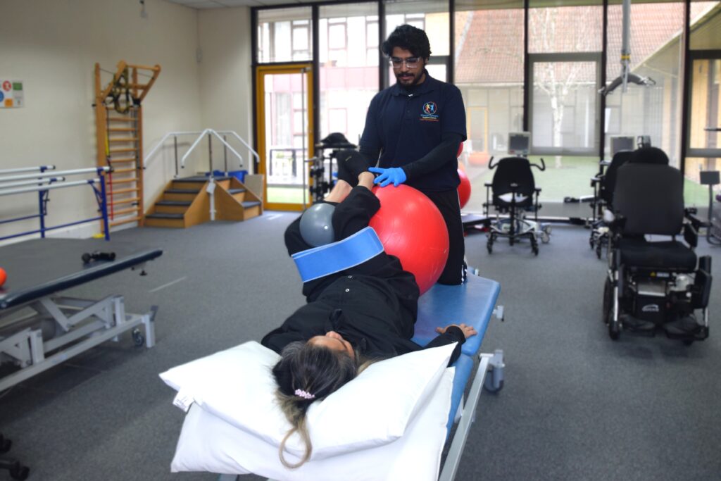A person lying on a treatment bed having physiotherapy. A physiotherapist is supporting them with an exercise.
