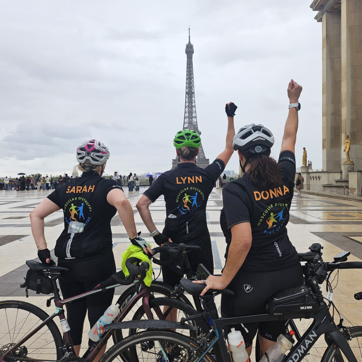 A group of people with their bikes standing in front of the Eiffel Tower with their arms raised in celebration,