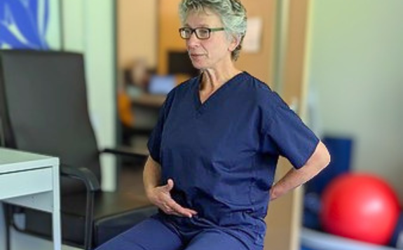 Person demonstrating a seated exercise in a therapy or rehabilitation setting.