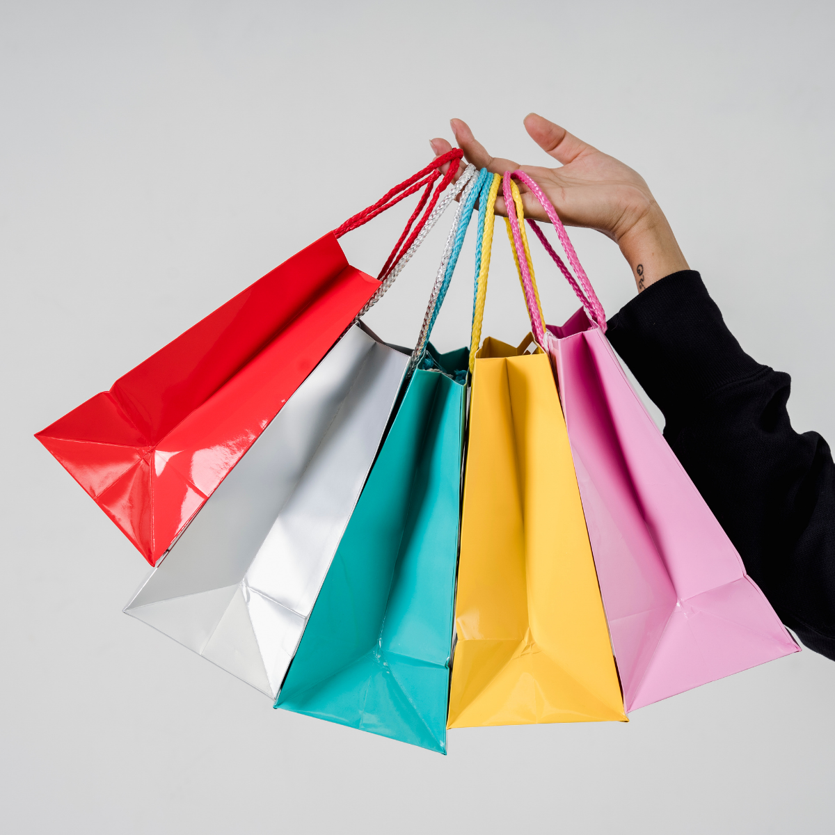 A hand holding some brightly coloured shopping bags.