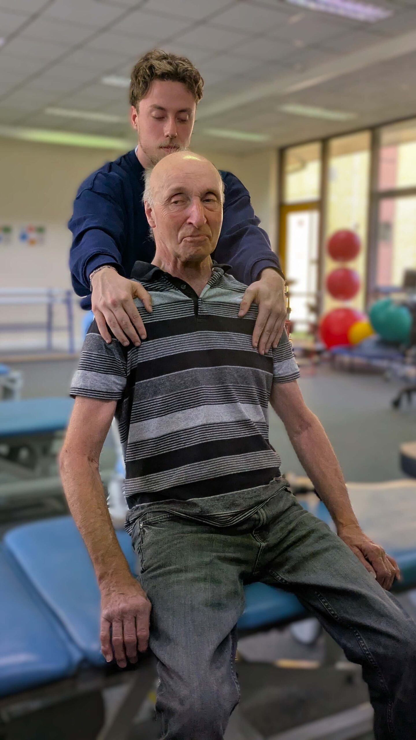 Student placement A physiotherapy student supports an older adult seated on a treatment table during a rehabilitation session in a therapy gym.