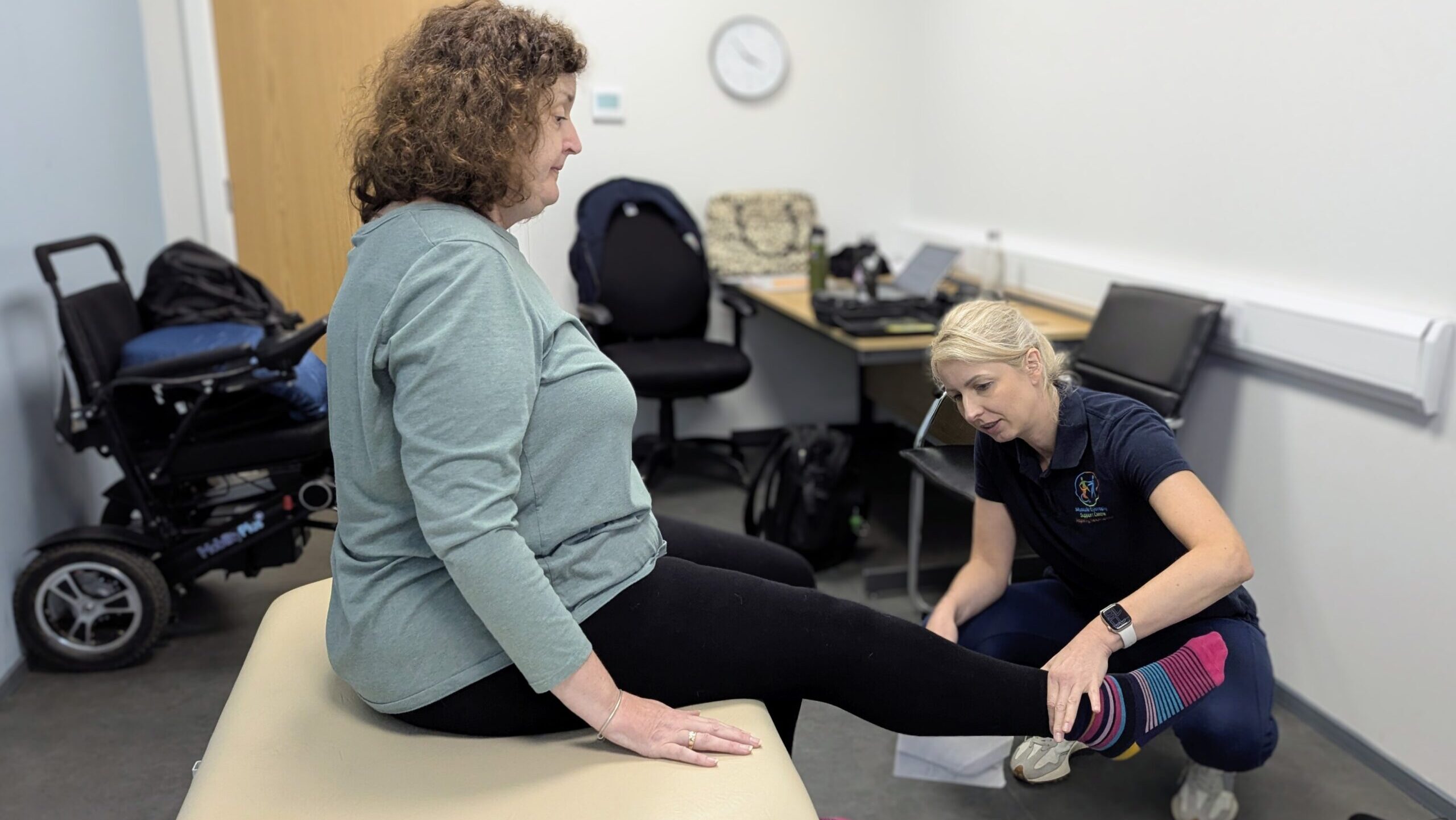 A physiotherapist performs manual therapy on a service user who is sitting on a treatment bed.