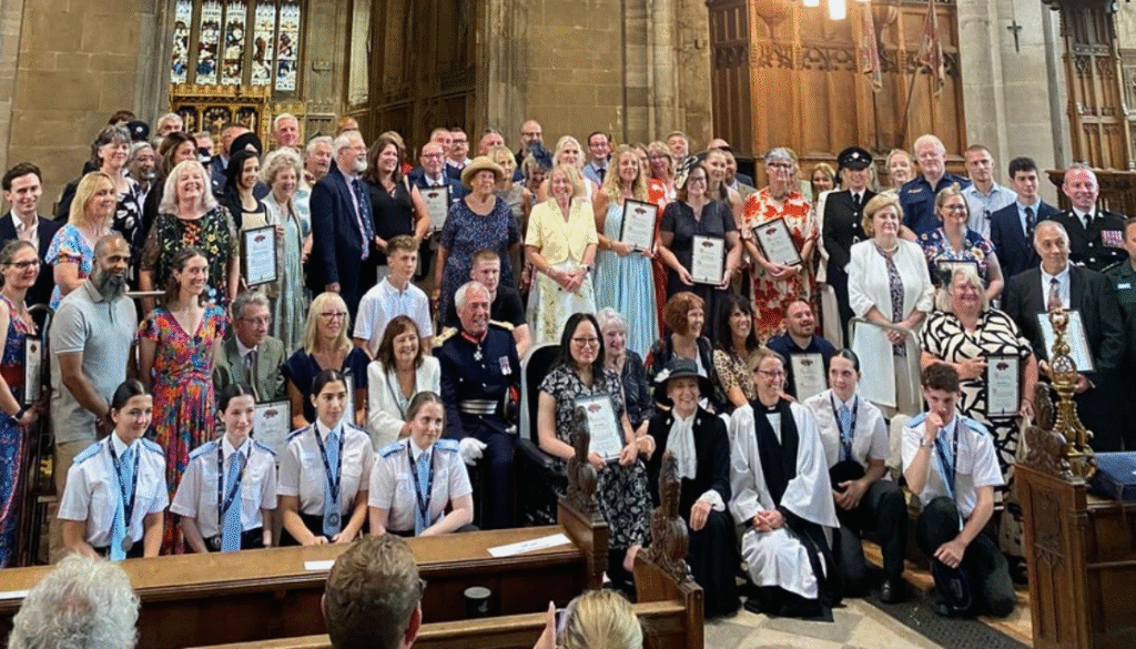 A large group of people standing, sitting, and kneeling at an awards ceremony . Many of them are holding certificates. Some are in ceremonial robes.