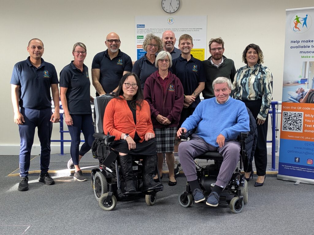 A group of people, some standing and some seated in powerchairs, in MD Support Centre's treatment area.