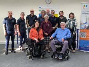 A group of people, some standing and some seated in powerchairs, in MD Support Centre's treatment area.